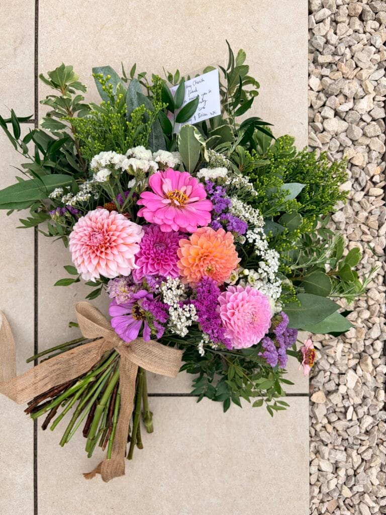 Hand-tied funeral sheaf with pink dahlias and zinnias, tied with a natural ribbon