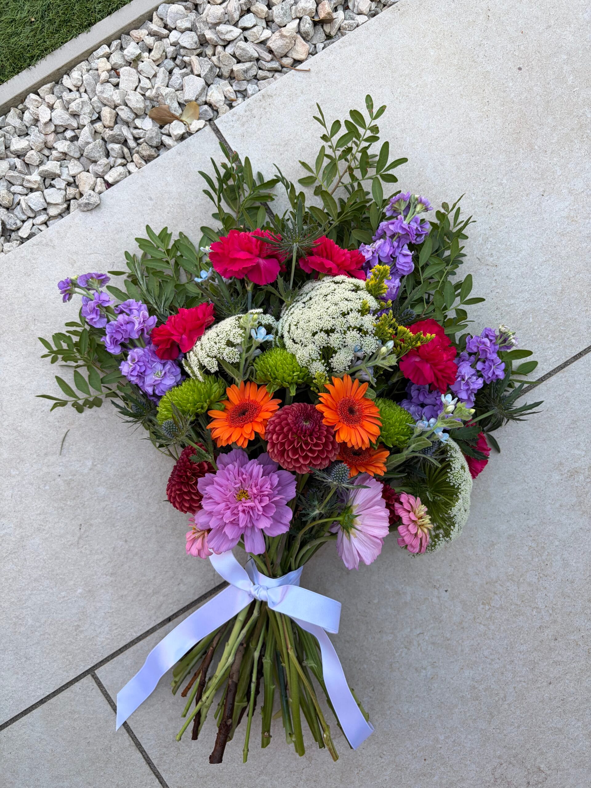 Bright hand-tied funeral sheaf with dahlias, gerberas and stocks, tied with a white ribbon