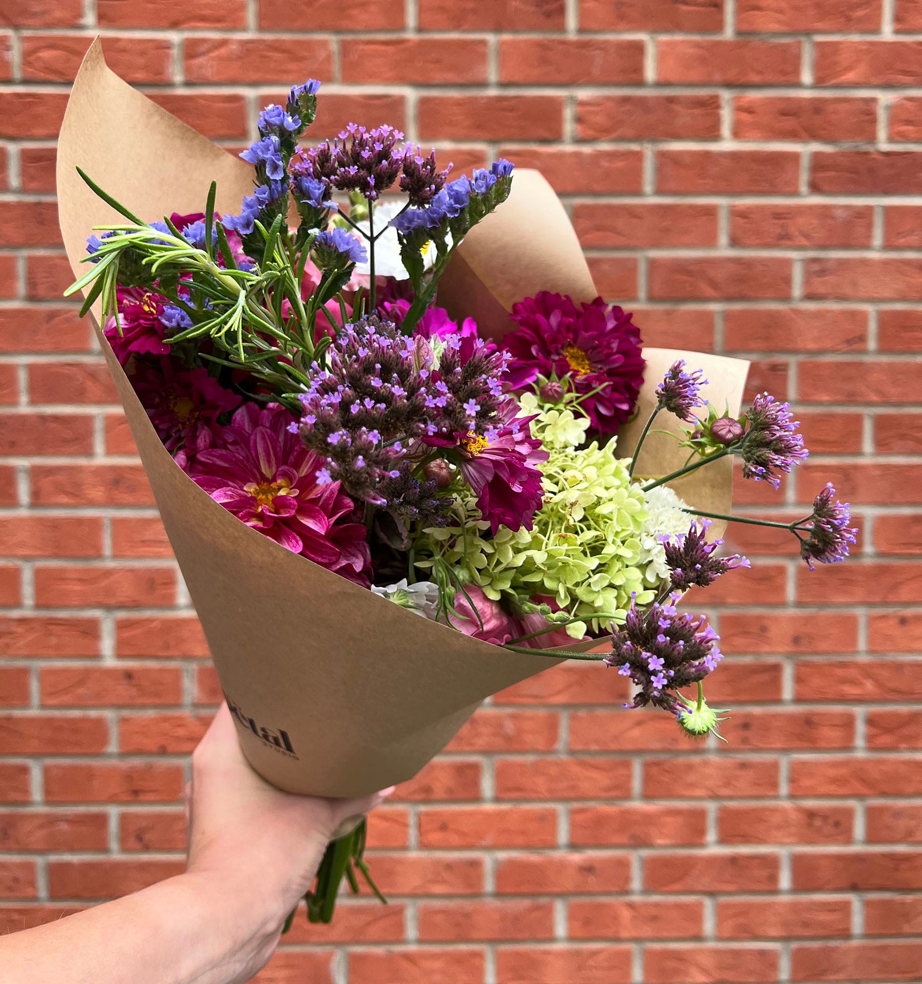 Hand holding colourful flower bouquet against brick wall.