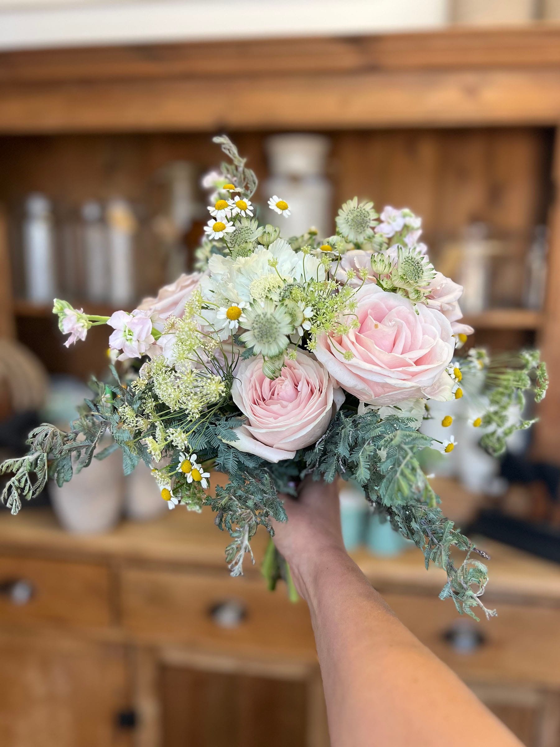 Hand holding pink and white flower bouquet.