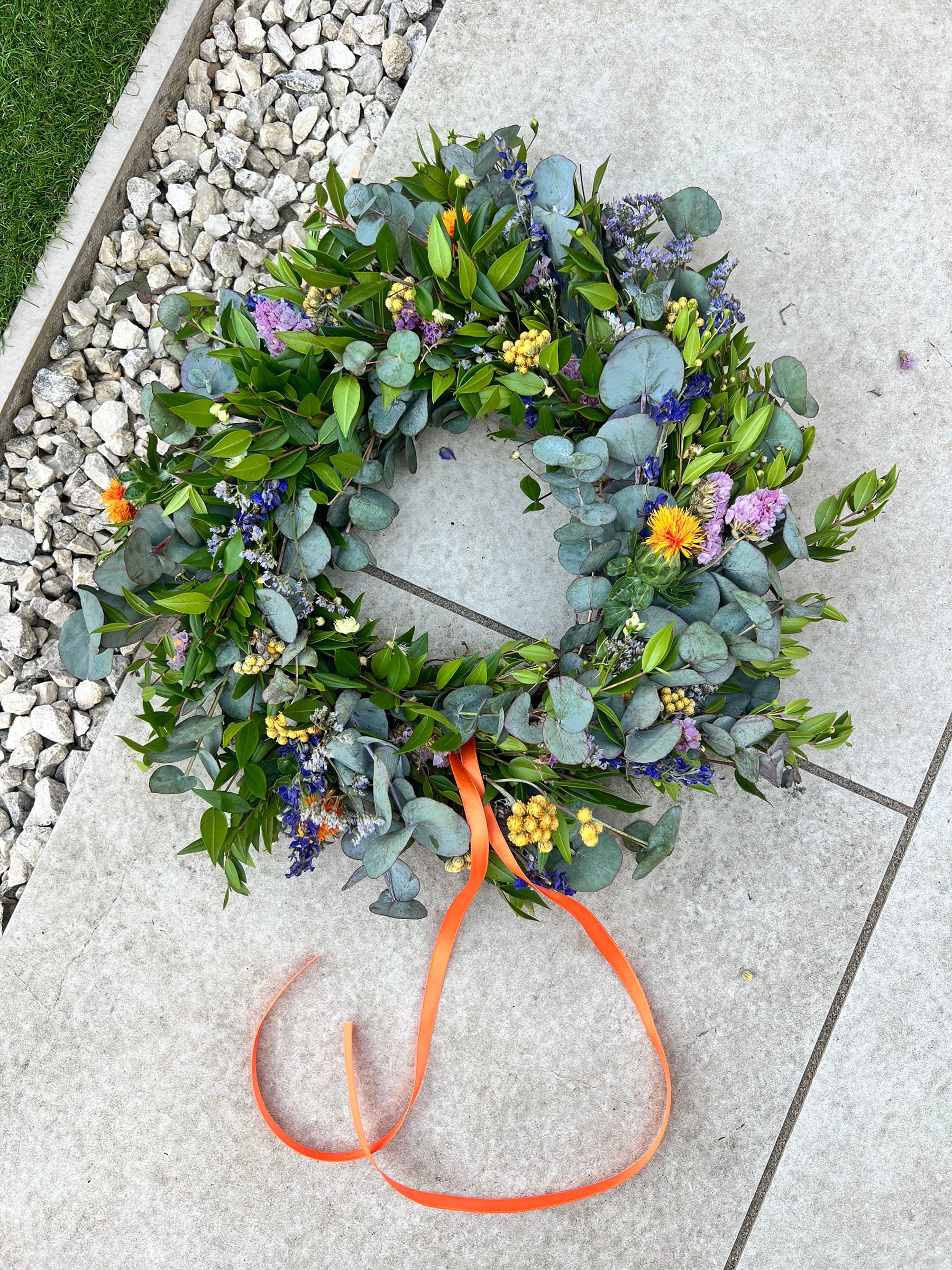 Floral wreath with orange ribbon on pavement