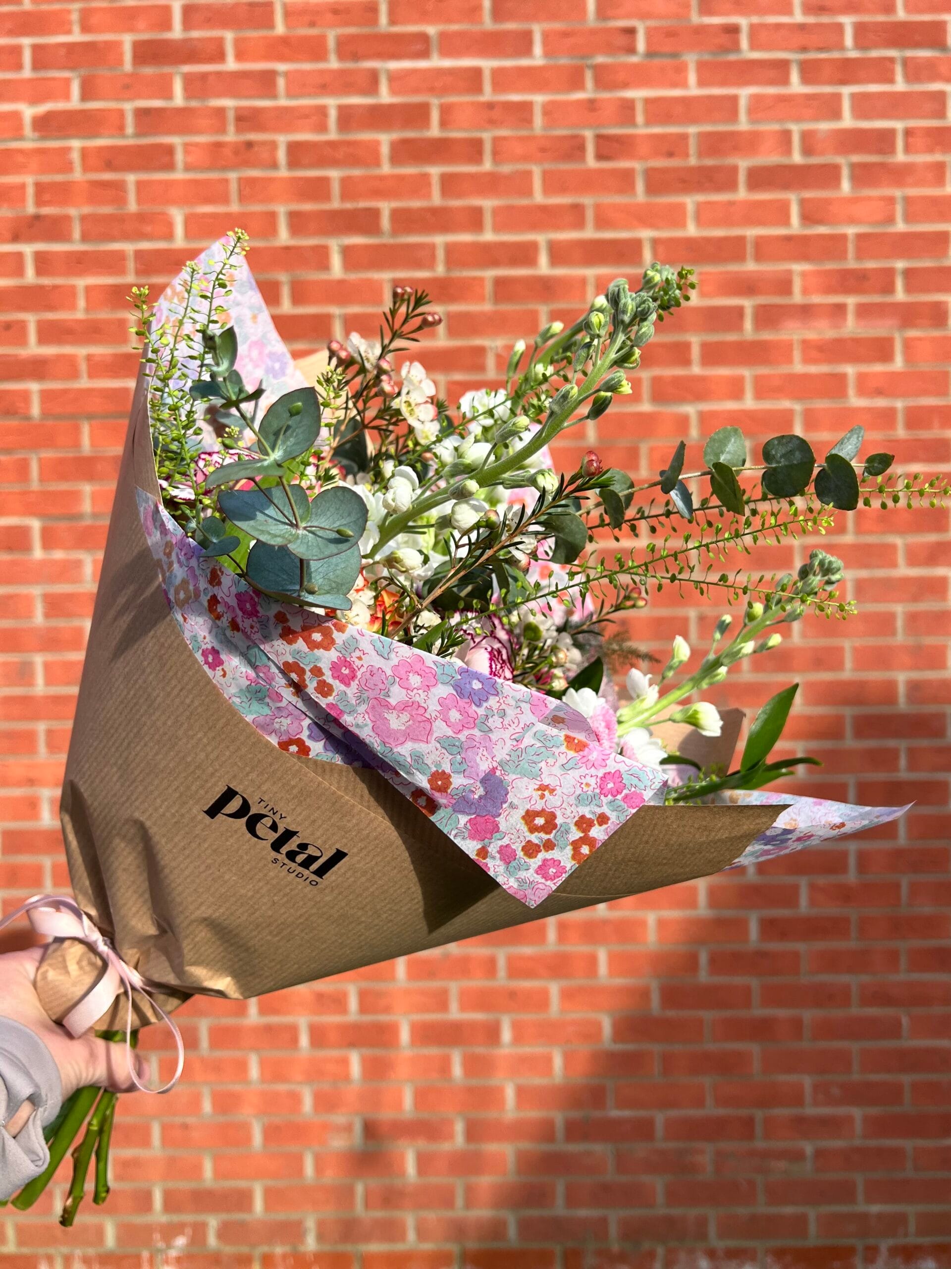 Hand holding colourful flower bouquet against brick wall.