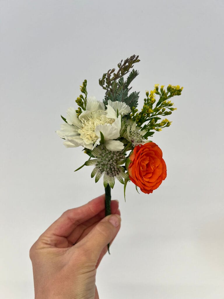 Hand holding small floral bouquet with orange rose.