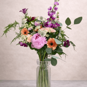 Vase of colourful, vibrant flowers on grey background.